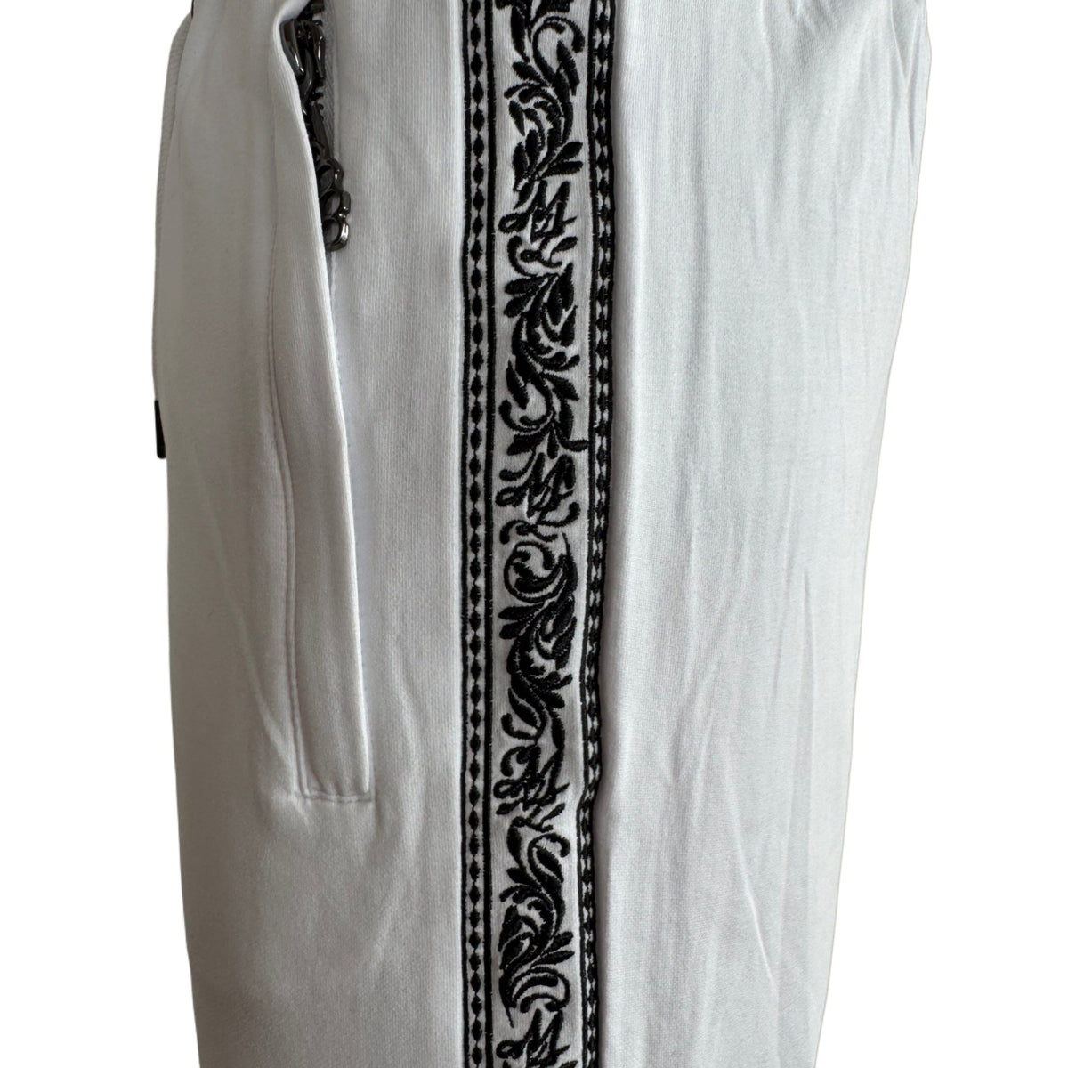 Close-up of the black embroidered Meander band and pocket zip on the white MVL shorts