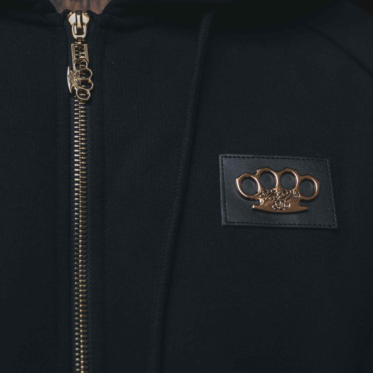 Primo piano del logo MVL dorato su patch in pelle e della zip dorata della felpa Meander