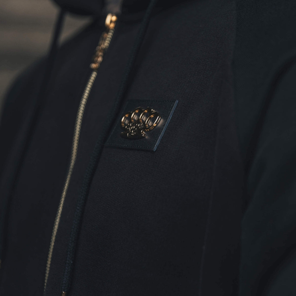 Primo piano del logo MVL dorato sul petto e della zip della felpa Meander nera