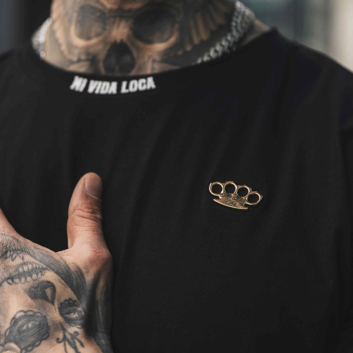 Primer plano del logo MVL dorado y el texto blanco Mi Vida Loca en el cuello de la camiseta FTS negra