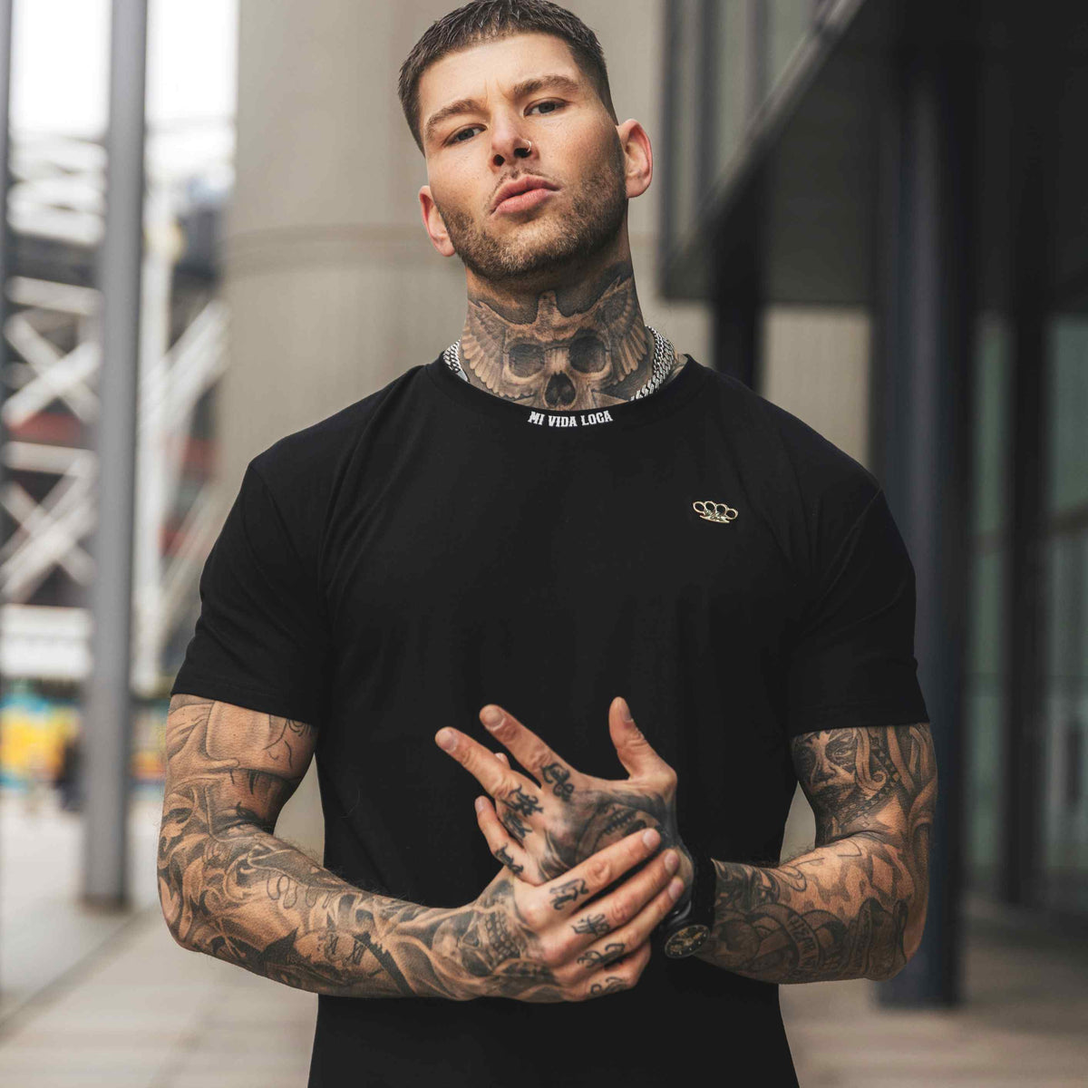 Modelo tatuado con la camiseta FTS negra, delantera, con las manos juntas delante del pecho