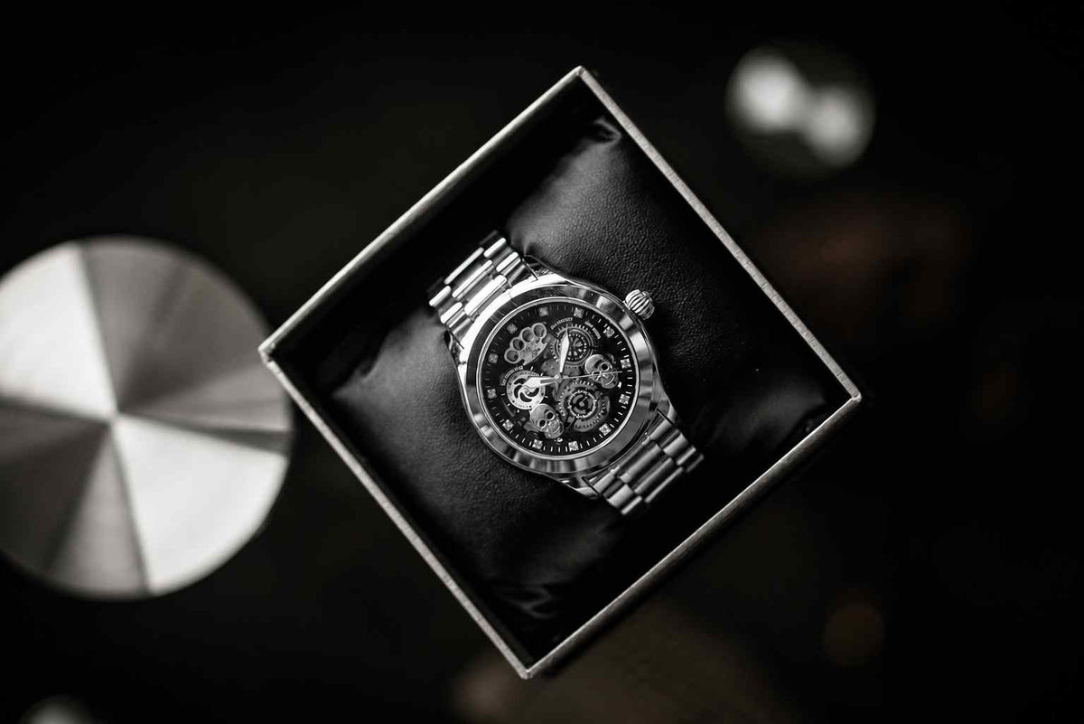 Reloj de pulsera automático MVL Double skull plateado en la caja de regalo abierta, visto desde arriba en un ambiente oscuro