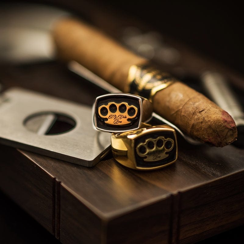 Chevalières MVL argentée et dorée à côté d'un cigare et d'un coupe-cigare sur bois