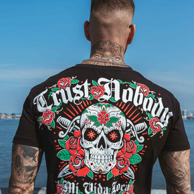 T-shirt Trust nobody flower skull noir porté par un mannequin, dos avec imprimé au bord de l'eau